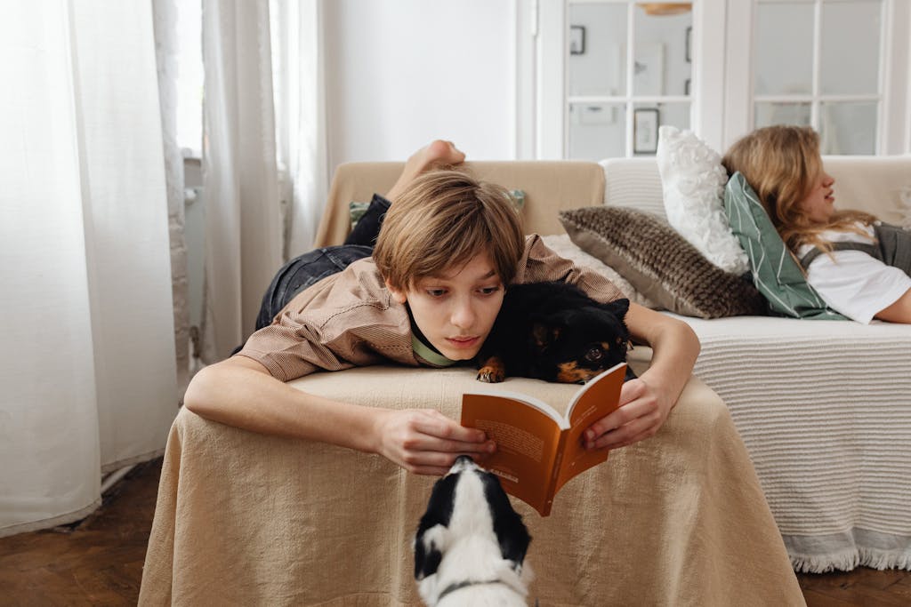 A teenager reading a historical fiction book on a couch with two dogs nearby, creating a cozy indoor scene.