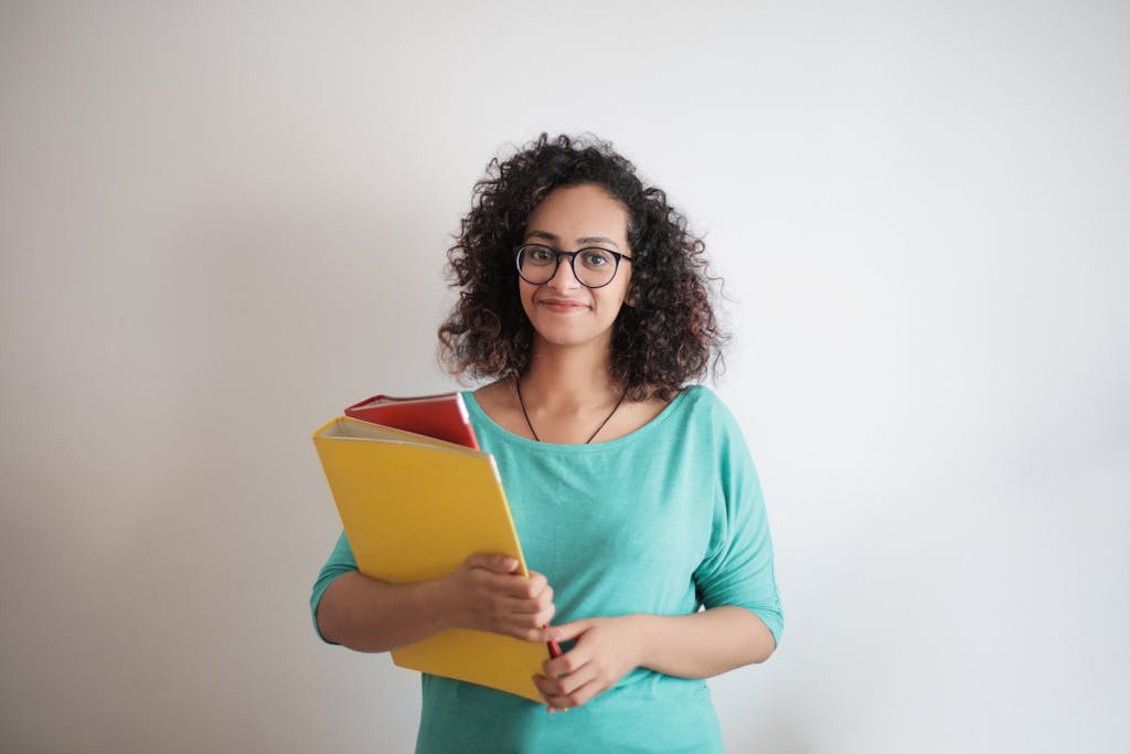 Portrait of a smiling woman with curly hair holding yellow folders in casual wear.
