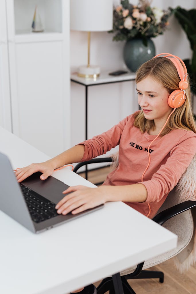 A teenage girl wearing headphones and using a laptop at home. Cozy indoor setup with casual attire.